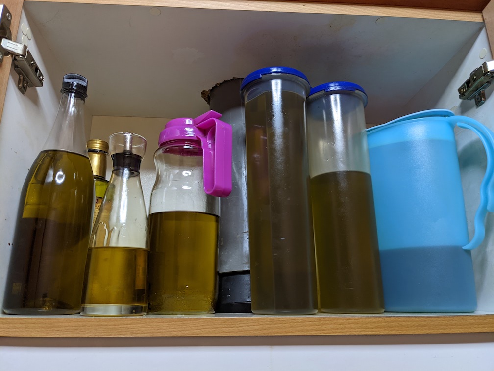 Photo of an open cupboard with 7 containers, each full of dark green olive oil